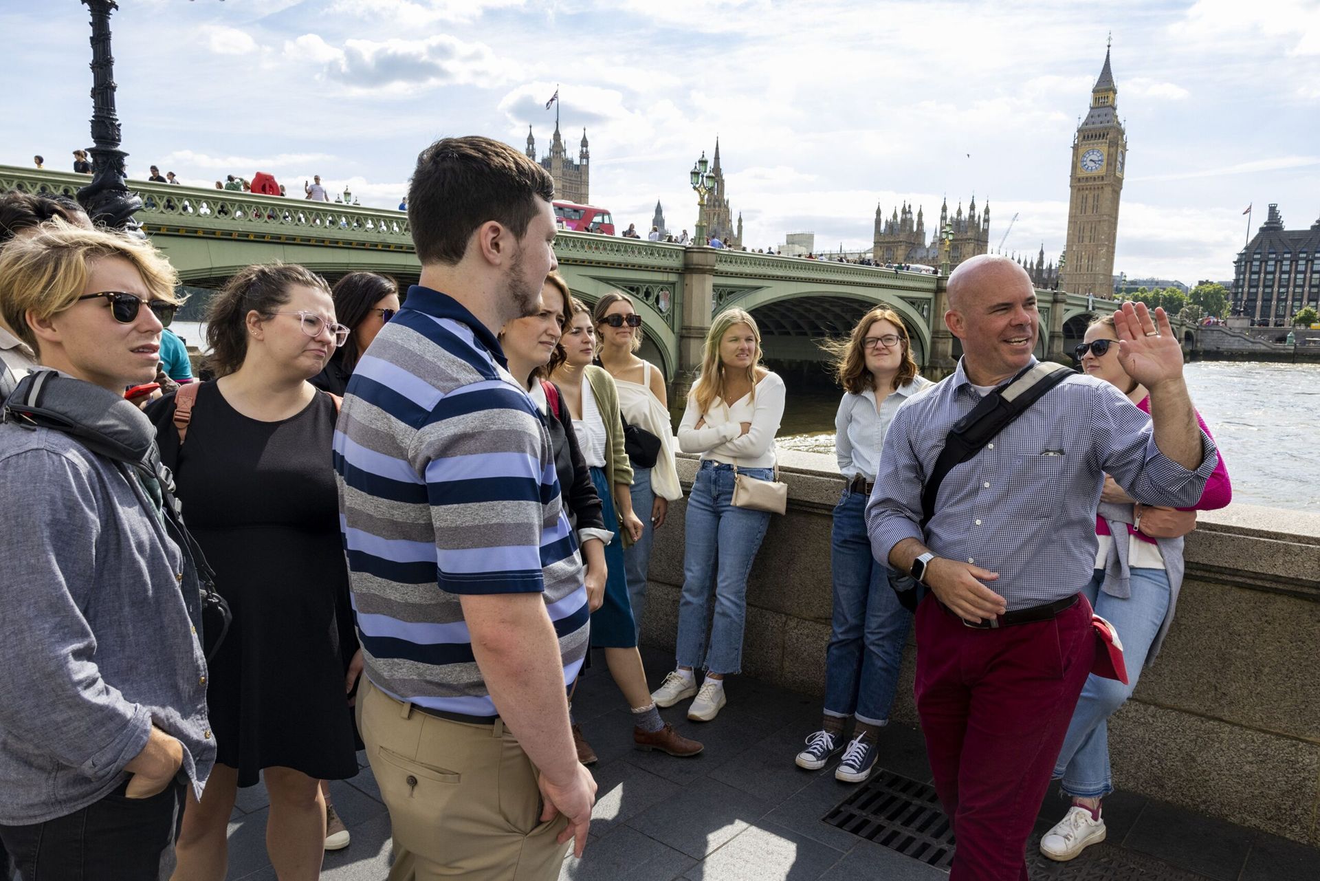 Man motions off-screen to a group of a dozen or so students. London’s Big Ben, Parliament, and Thames River are in the background.