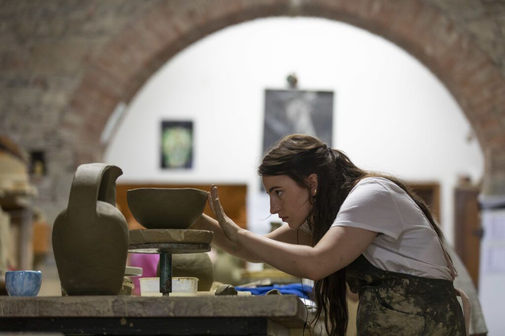 A female student concentrates intensely on creating a bowl in a pottery studio.