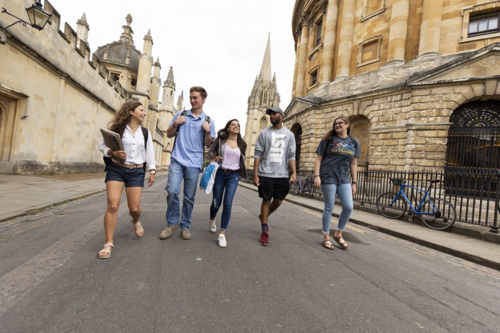 A group of five students walks towards the camera as they stroll through a European street.