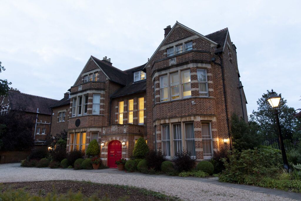 A brown stone house is lit warmly from the outside as dusk approaches outside.