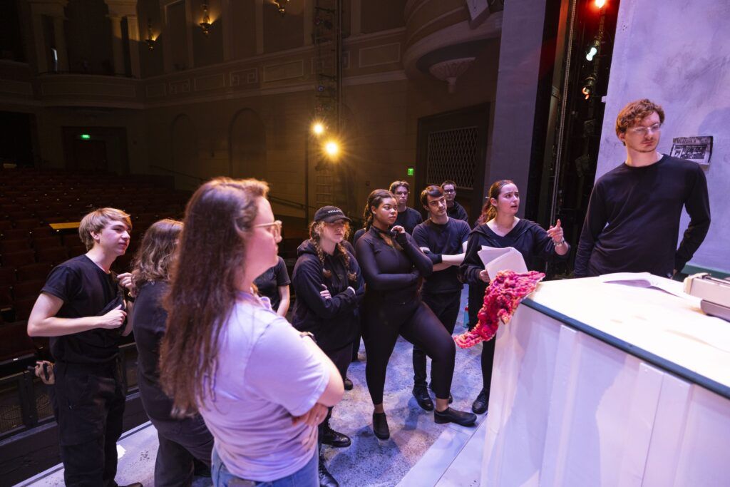 The crew for Little Shop of Horrors meets on stage for dress rehearsal. Most of them are dressed completely in black.