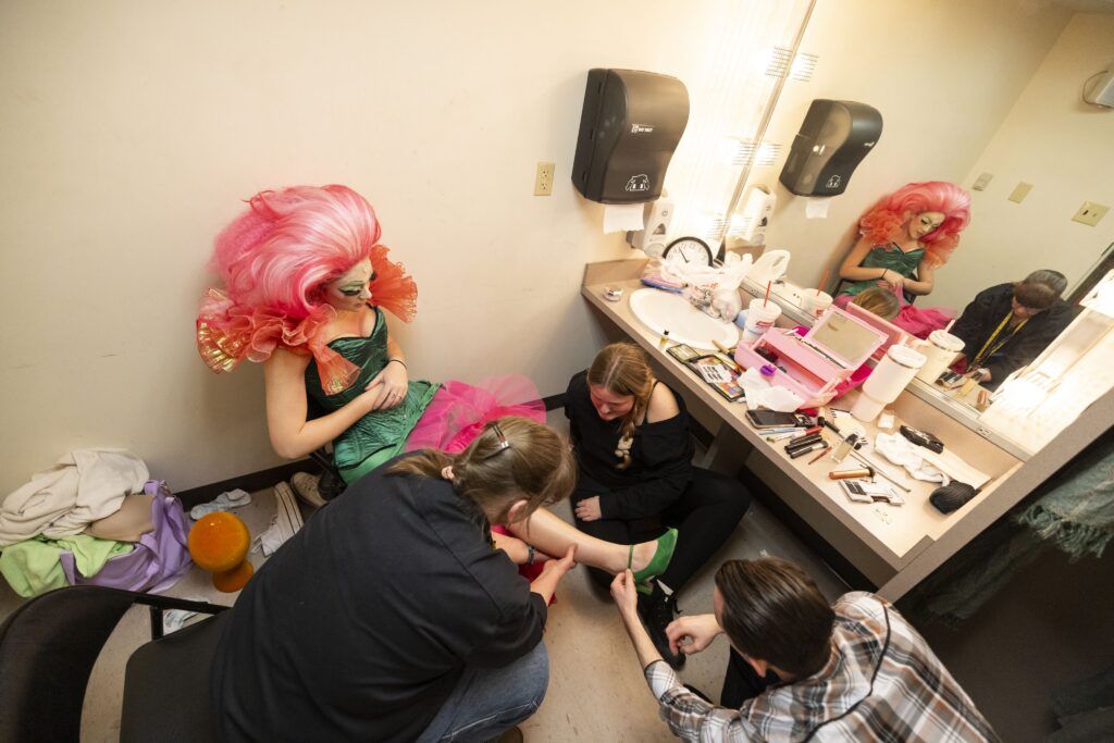 An actor playing Audrey 2 gets helped into their costume by three people in UGA's theatre department.