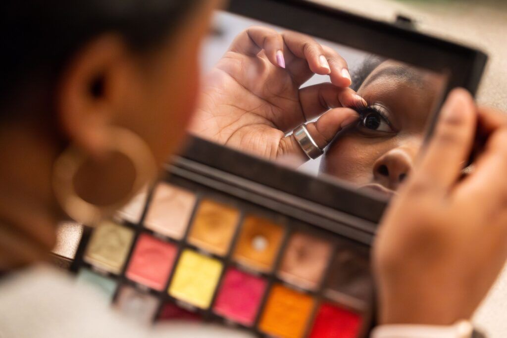 An actor looks at her reflection in a long rectangular compact makeup mirror as she adjusts her eyelashes.