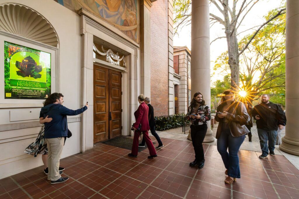 Several people enter a theatre during the opening night of Little Shop of Horrors.