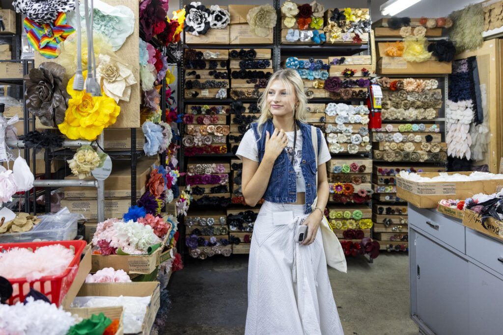 A young woman in a white skirt and jean vest studies the many colorful flowers in a store in New York's Garment District.