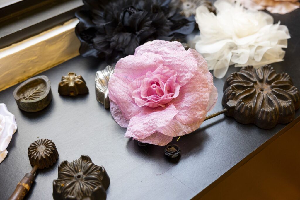 A closeup of a worktable covered in fabric flowers. There are also dark brown tools shaped like different leaves and flowers.