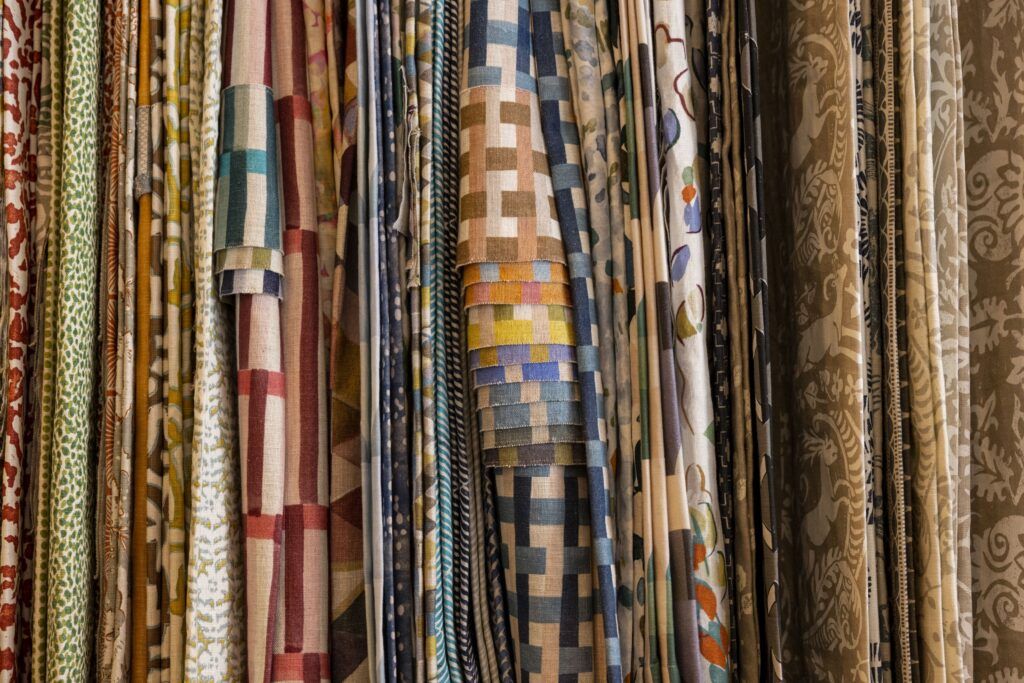 A closeup of several different types and color of fabric. They are hanging from an unseen object and neatly lined up.