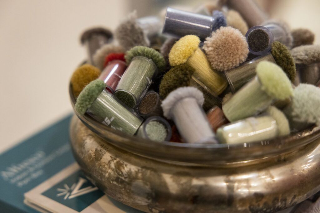 A closeup of a bronze bowl filled with different colors fabric samples. The samples are shaped into small tufts and wrapped in plastic.