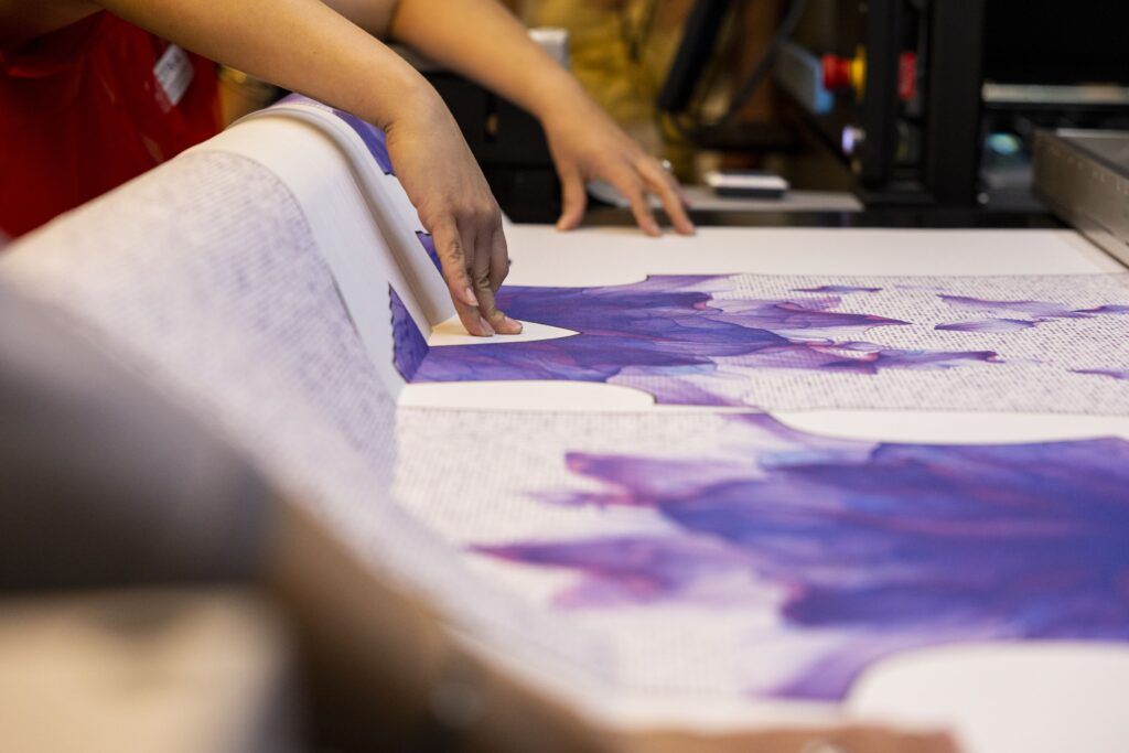 A closeup of a pair of hands against purple and white fabric. The fabric is stretched over a table.