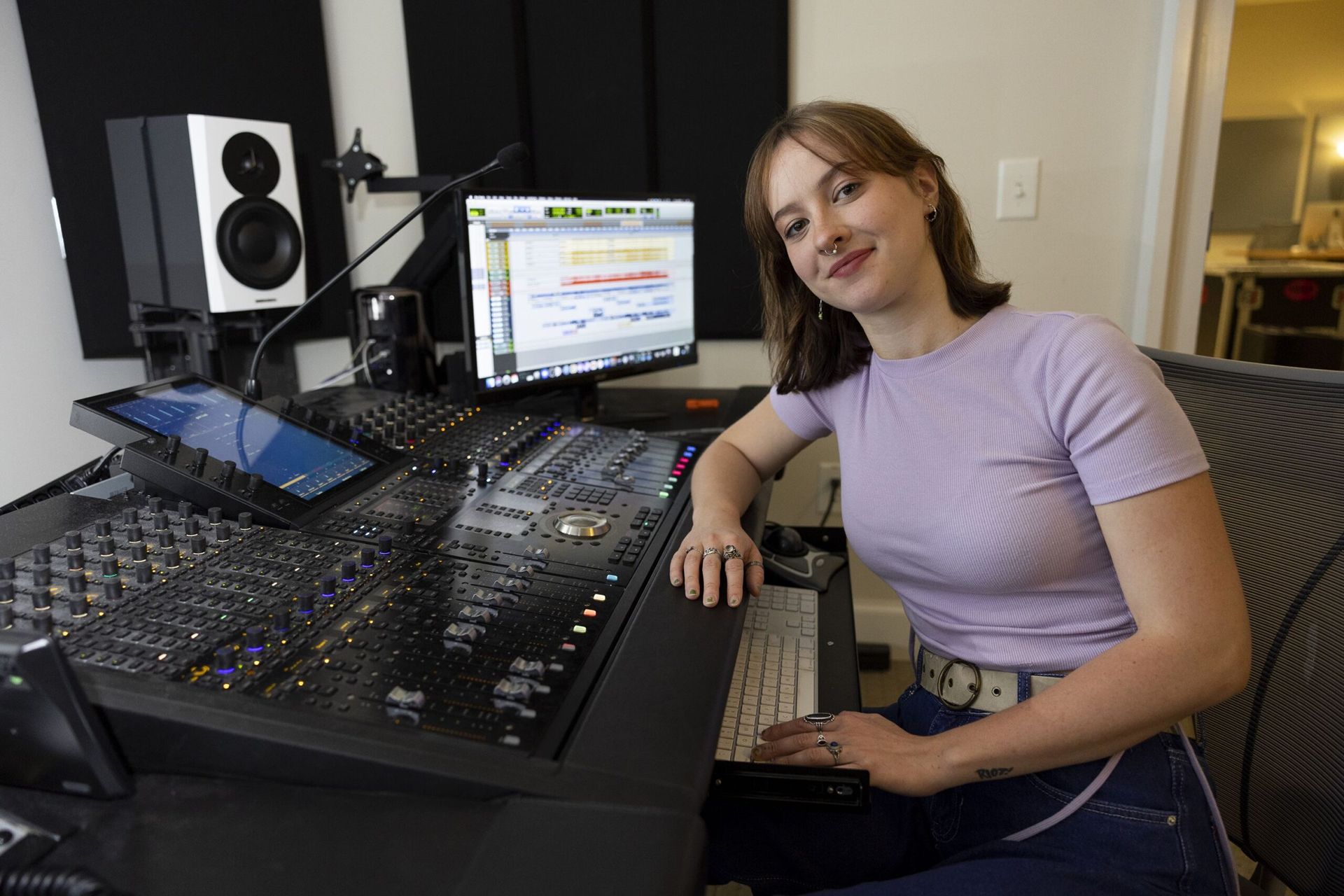 A woman in light purple shirt in a production studio's music room sits in front of a modern sound board.