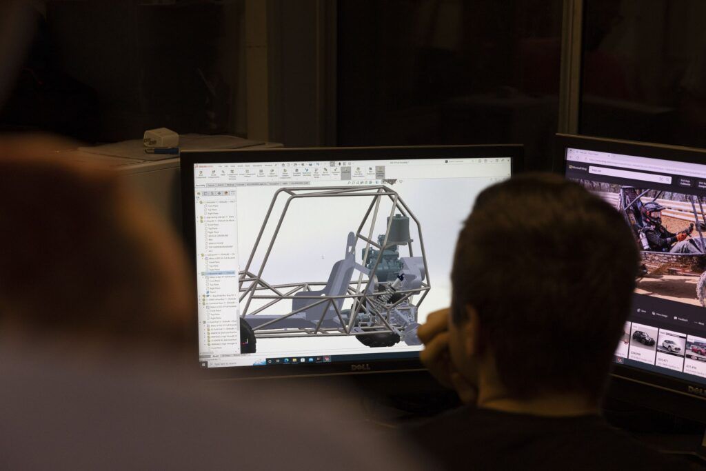 The back of a student’s head is visible as he looks at a computer screen where a car’s frame is being designed.