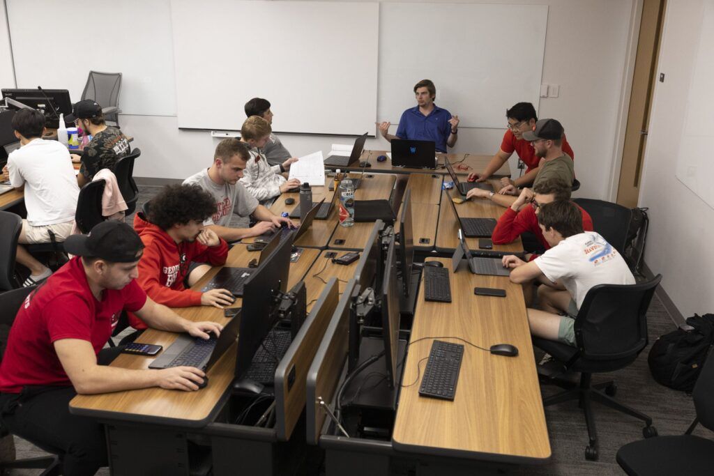 10 students sit around several long tables, looking at computer screens as they work on designing a Formula SAE vehicle