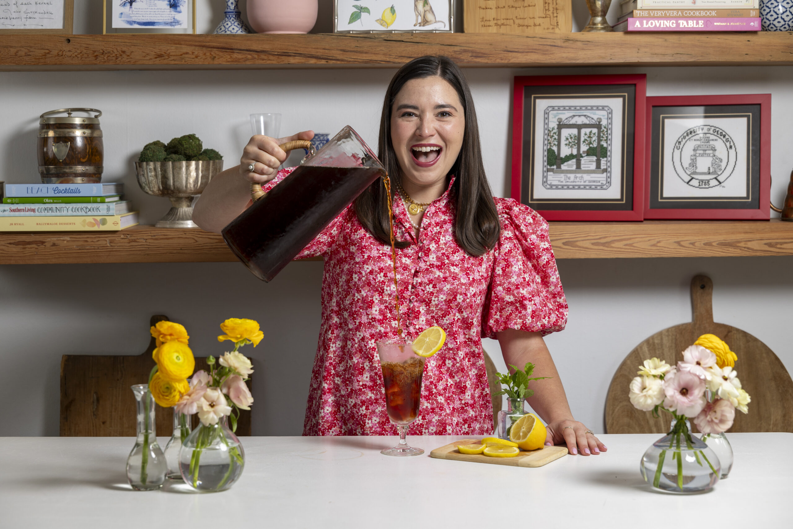 Ivy Odom in a bright pink dress smiles widely while holding a glass of iced tea.