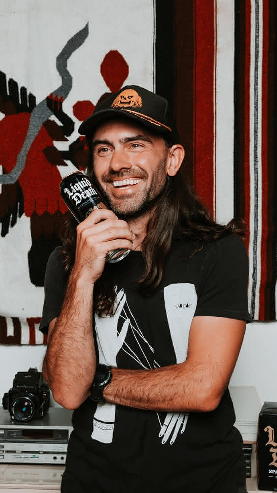 Portrait of Andy Pearson, wearing a cap and smiling with a can of Liquid Death