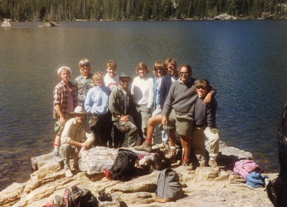 In an old photo, 11 people in hiking clothes pose in front of a lake.