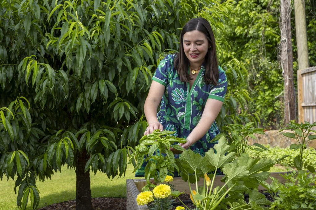 Ivy Odom, a UGA graduate, wears a bright blue and green dress tends to plants in a greenhouse.