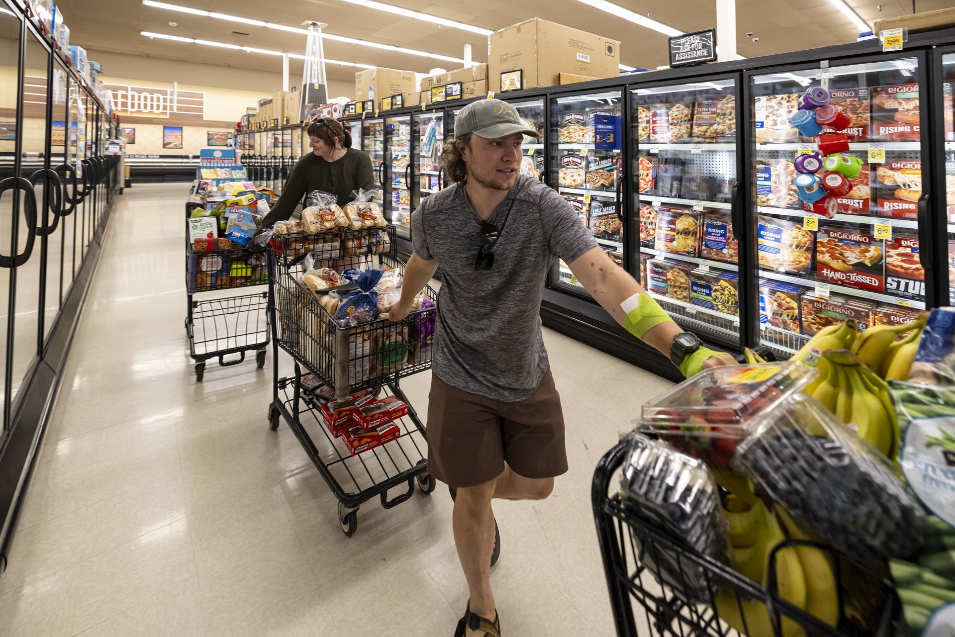 A man and a woman haul three full grocery carts down the freezer section of a grocery store.