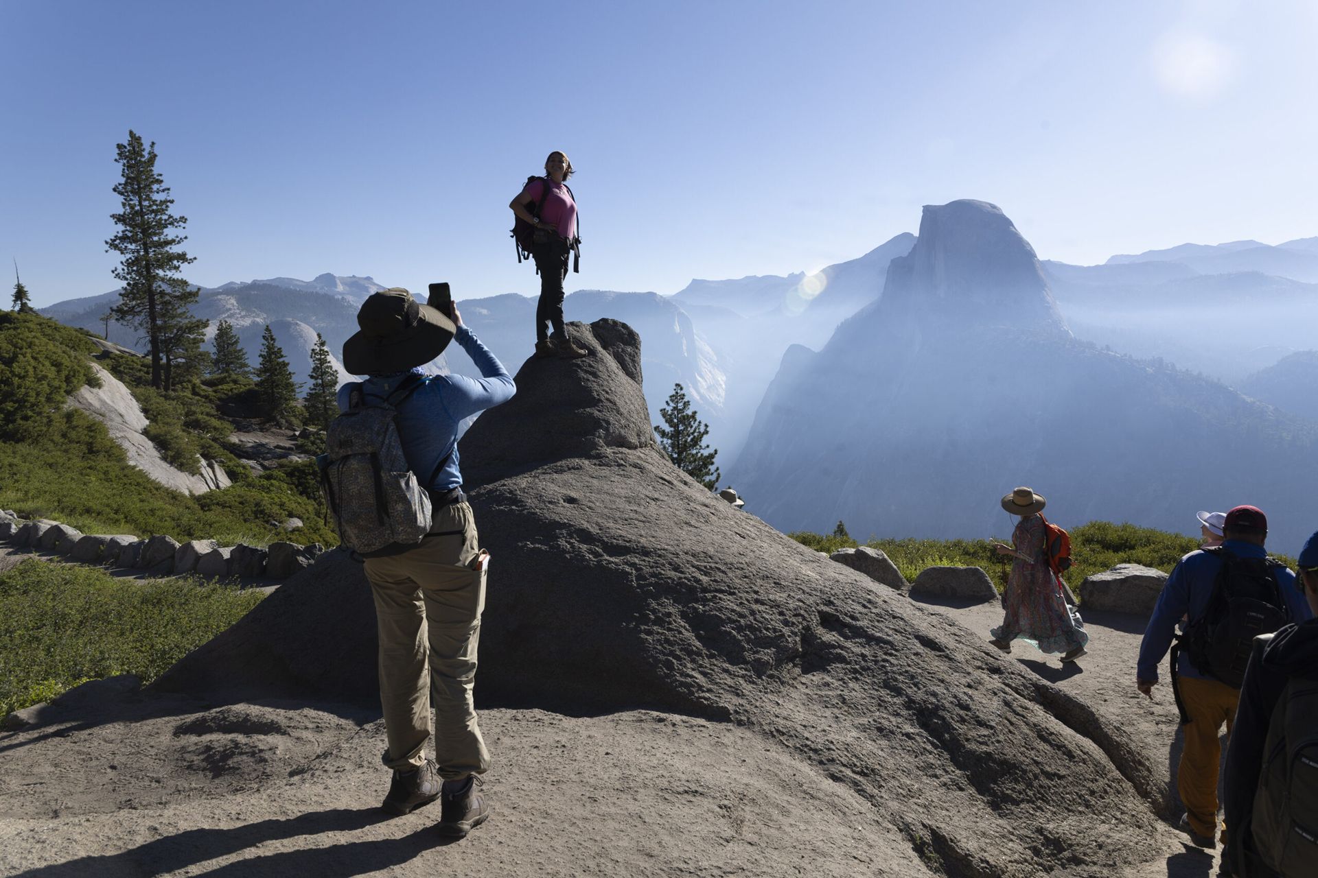 A backlit student stands on a rock posing for a photo with a mountainous background at Yosemite National Park.