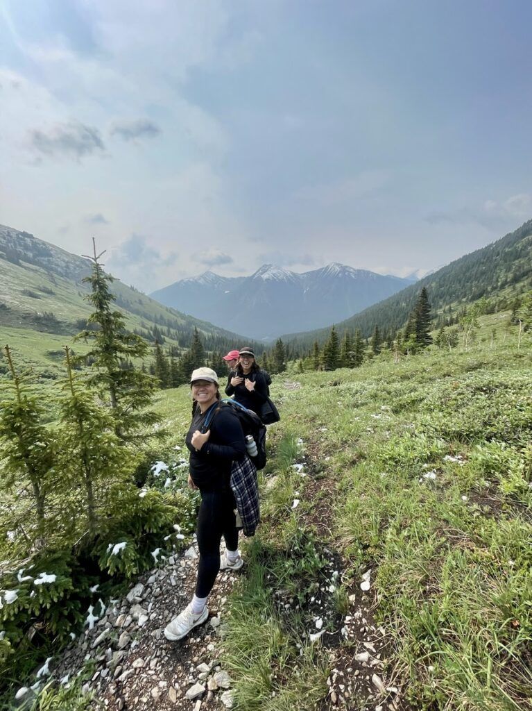 A smiling group of young women hike across a grassy mountain.