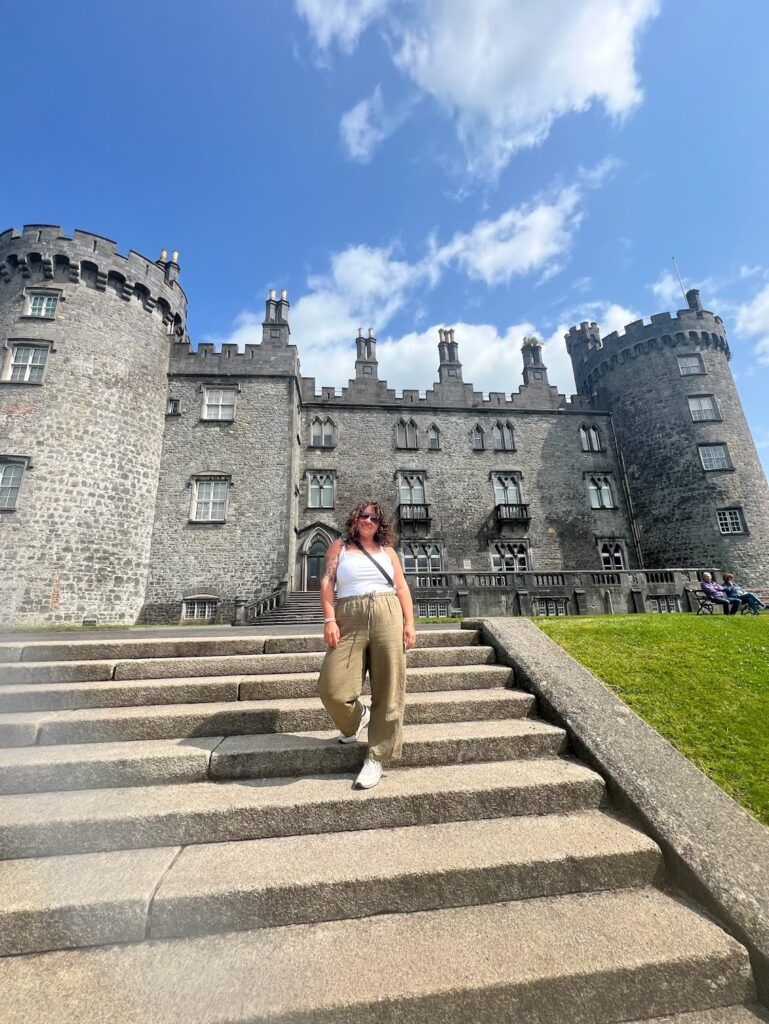 UGA student Julianne O’Connell in a white top and brown pants as she stands confidently on the steps leading up to a medieval style castle.