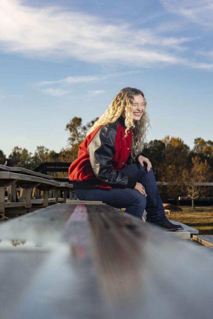 UGA student Caitlin Lyons sits on the bleachers and laughs under a bright blue sky.