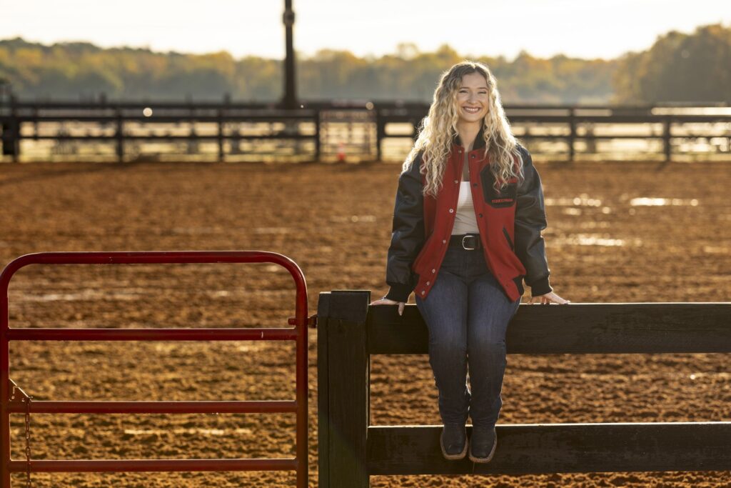 Caitlin Lyons, a student and equestrian at UGA, sits on top of a fence in the middle of a ranch.