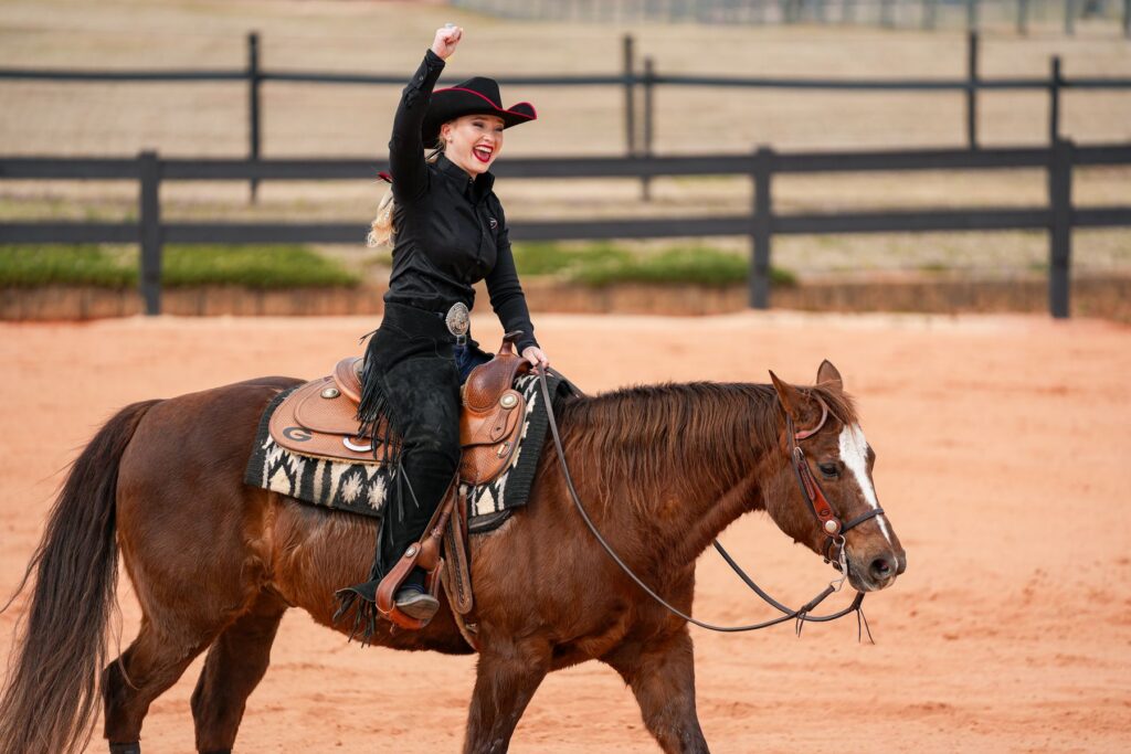 UGA student Caitlin Lyons raises her fist in a victory pose while riding her horse during a horseback riding competition.