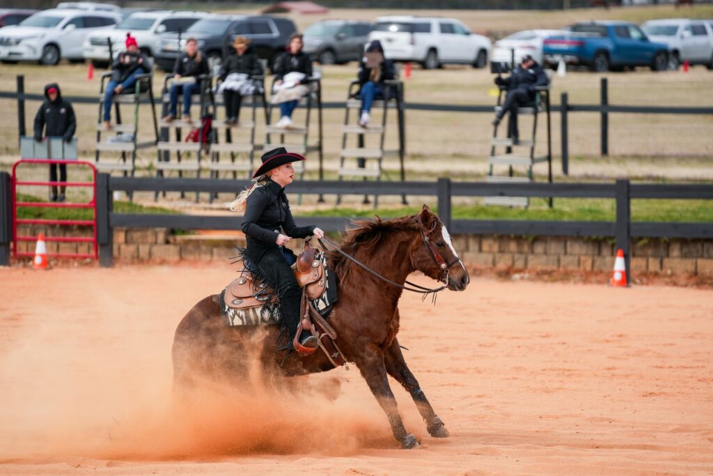 Caitlin Lyons, a student at UGA, competes in a horseback riding competition while judges look on from the sidelines.