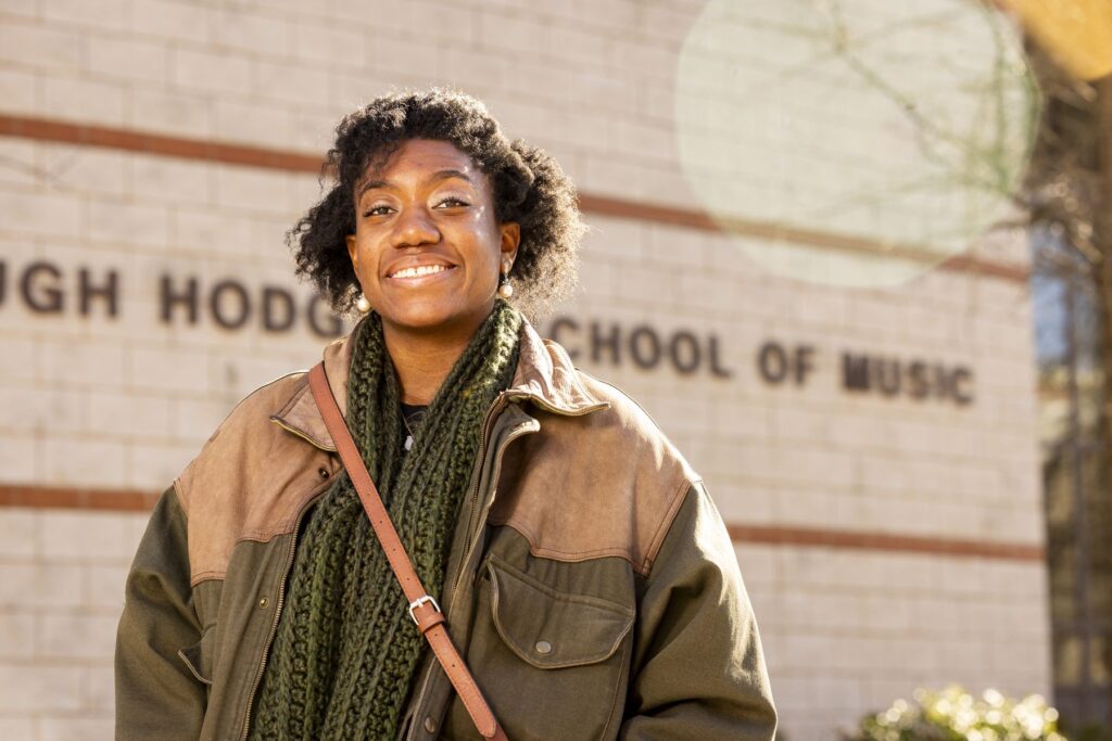 A closeup photo of Asia Simone Passmore, a graduate student at UGA. She is wearing a dark green jacket and standing in front of the Hugh Hodgson School of Music.