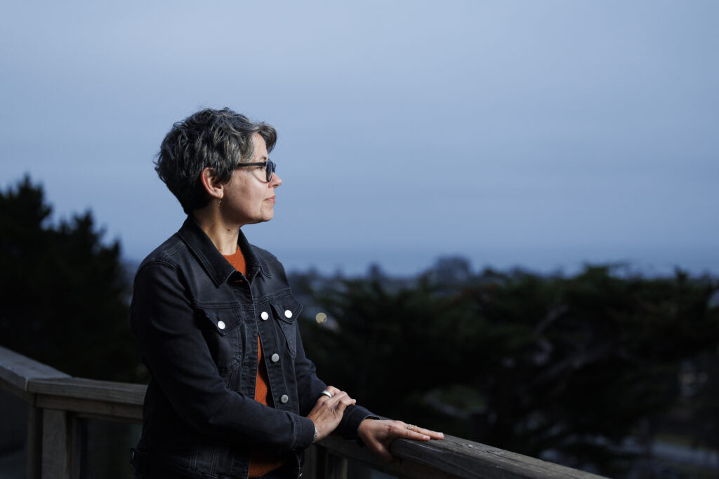 A closeup of dire wolf researcher Beth Shapiro outside on a deck as she stares off into the distance.
