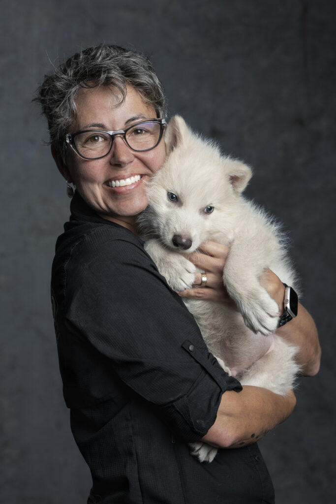 Beth Shapiro embraces a white wolf pup in a photo studio setting.