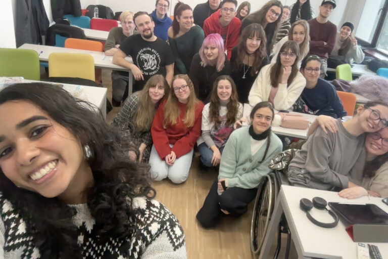 A large group of UGA honors students kneel in a classroom and smiles at the camer.