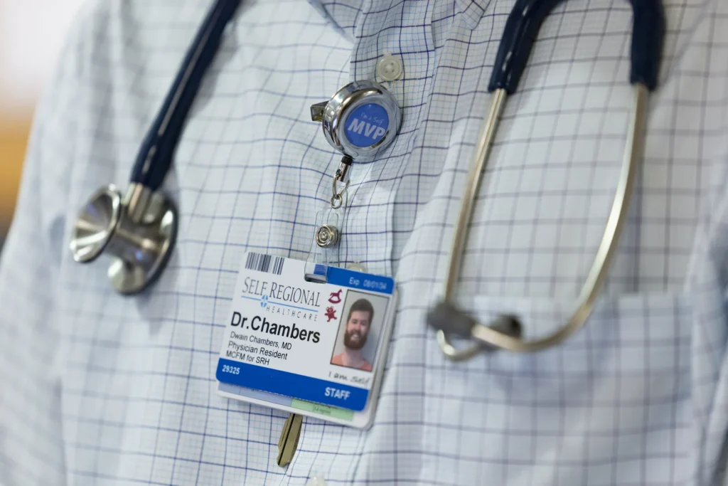 A closeup of someone wearing a checkered shirt with a stethoscope around their neck. They are wearing a hospital badge that reads Dr. Chambers.