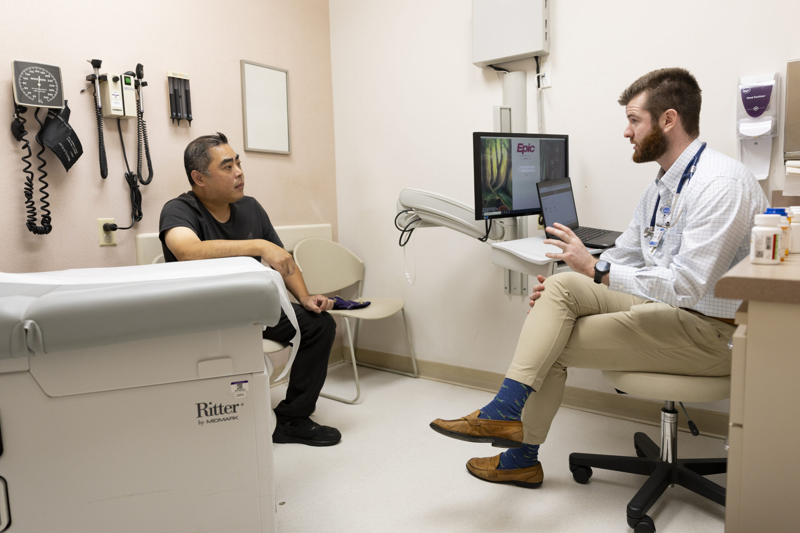 A patient in black clothing talks with his doctor, Chip Chambers, in an examination room.