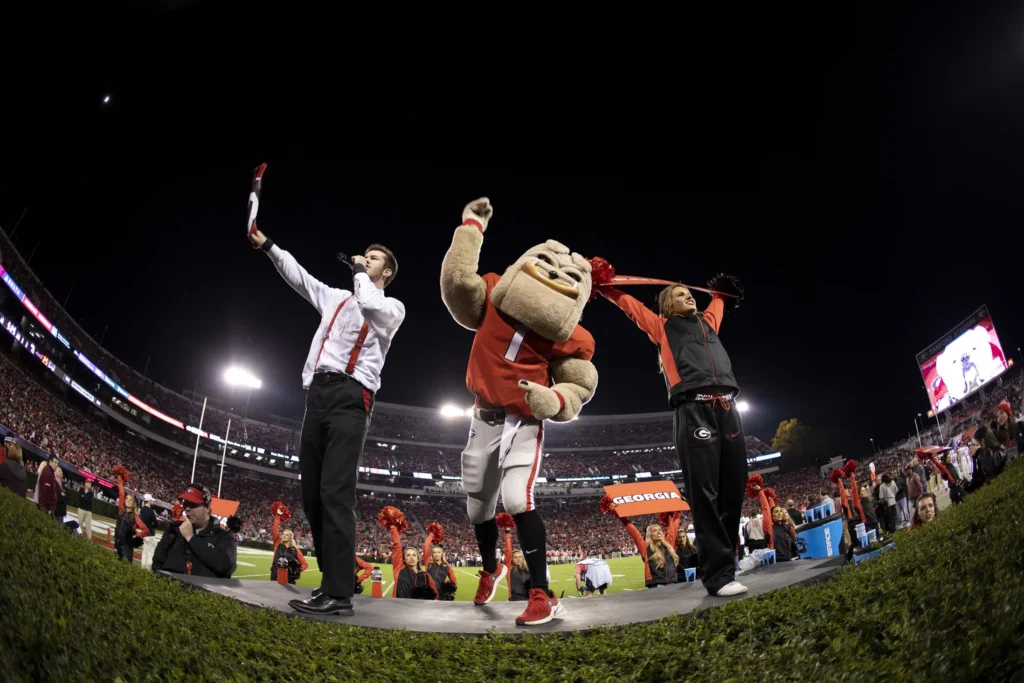 A fisheye view of a person dressed as a bulldog mascot, a young Chip Chambers as Mic Man, and a student in black and red clothing.