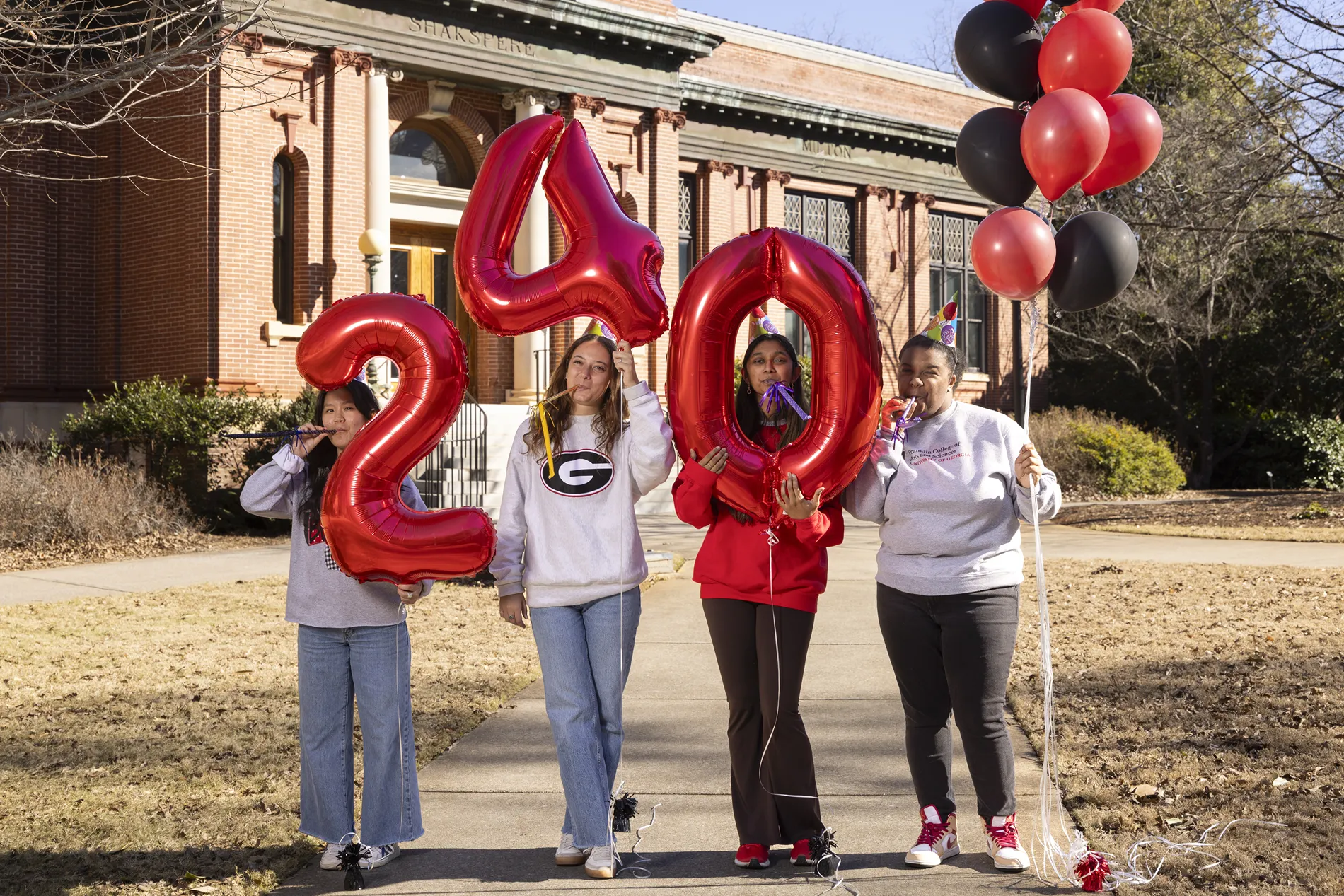Four UGA students, including Swetha Pendela, stand outside a campus building with red ballons reading 2, 4, and 0.