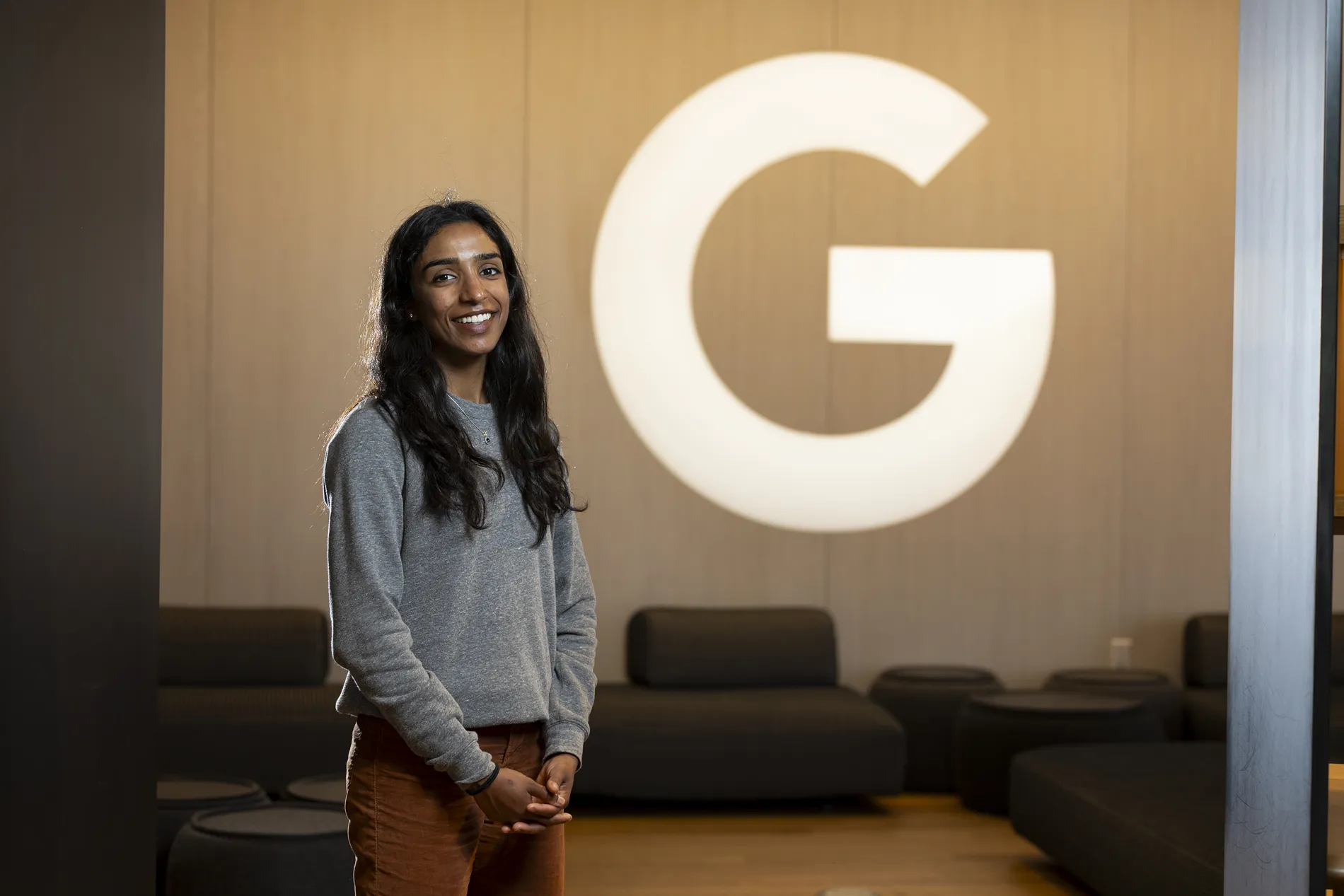 A young woman poses in a room with a brightly lit "G" behind her.