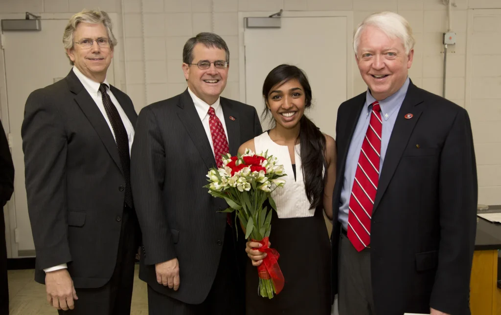 A young woman poses with three older men. She is holding flowers.