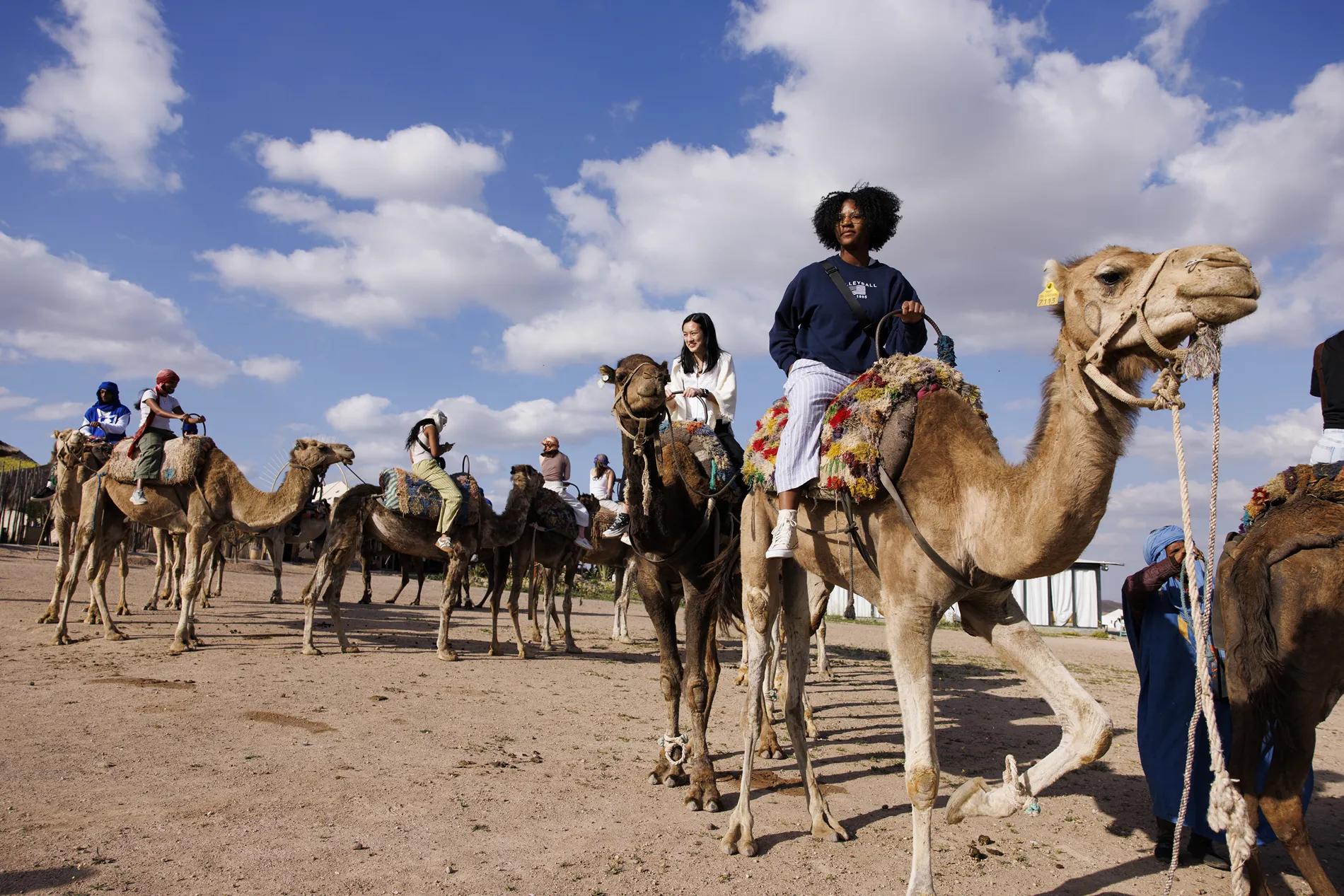Students ride camels through the desert.
