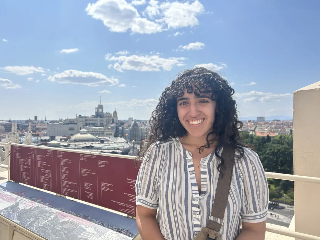 A woman poses in front of a city skyline on a sunny day.