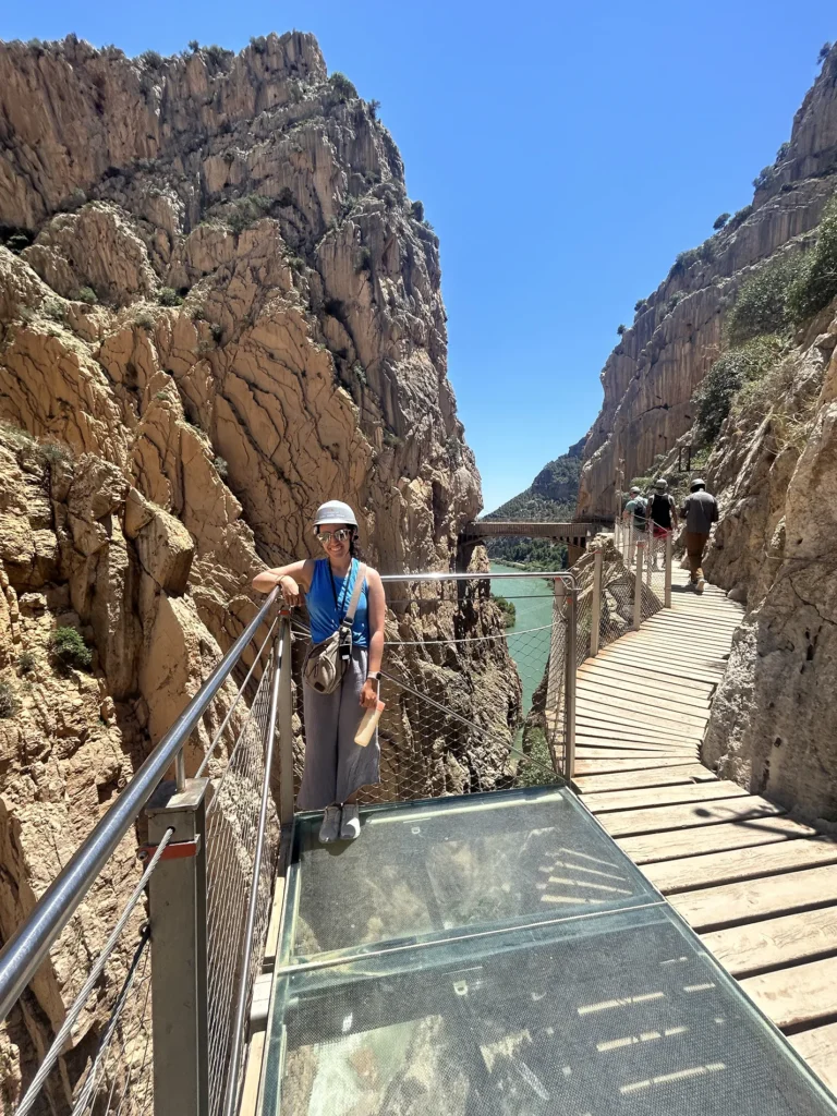 A woman stands on a glass and metal bridge in a rocky canyon.