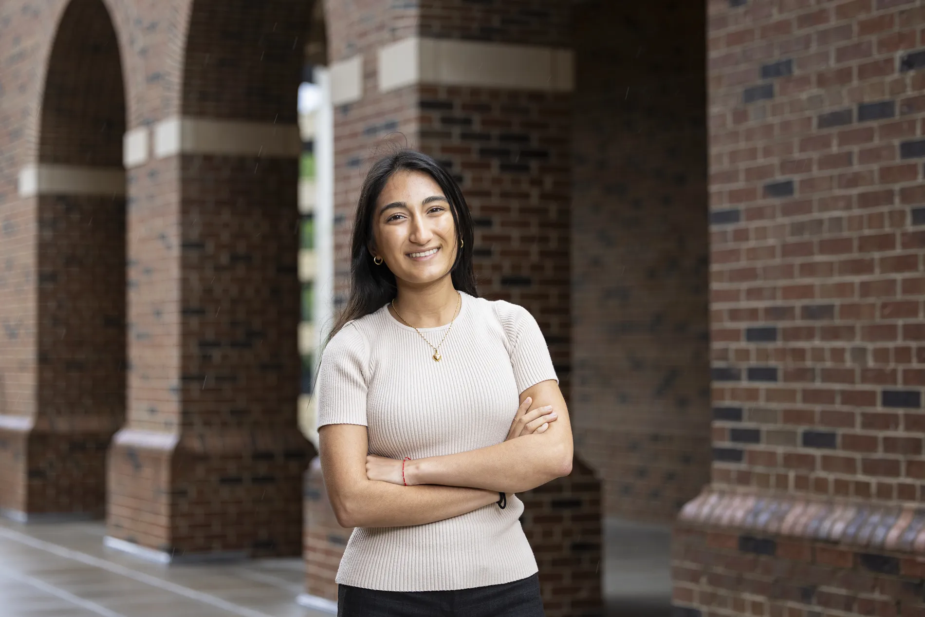 A young woman stands with her arms crossed outside of an academic building.