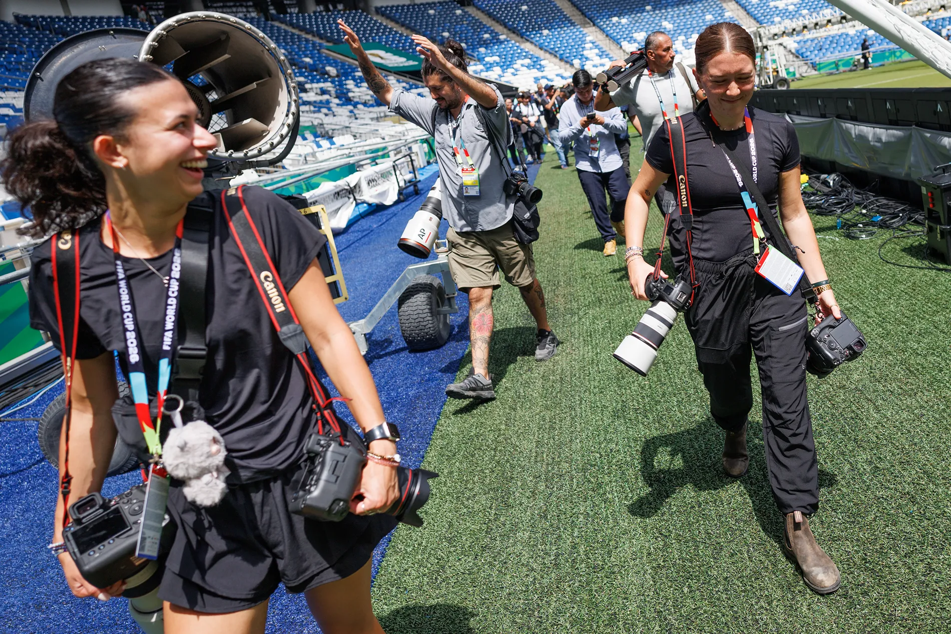 Several people with camera equipment walk across green turf.