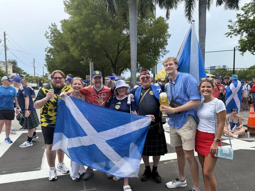 A group of people stand in a crosswalk and hold a blue flag with a white "X" across it.