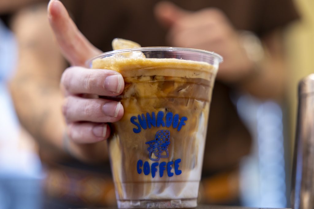 A closeup of a plastic cup filled with coffee. The cup has a "Sunroof Coffee" logo and text.