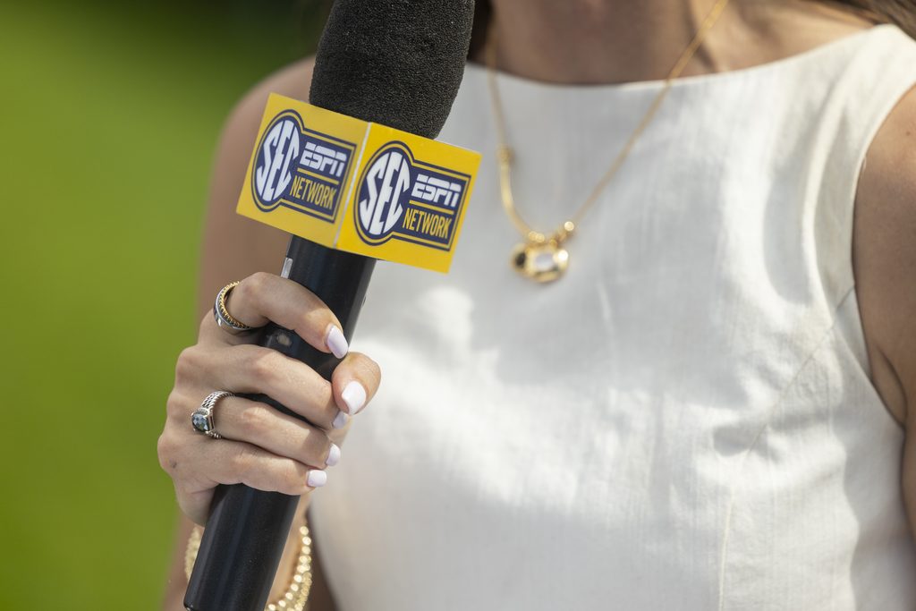 A closeup of a hand holding a microphone with a blue and yellow box around it that reads "SEC ESPN Network."