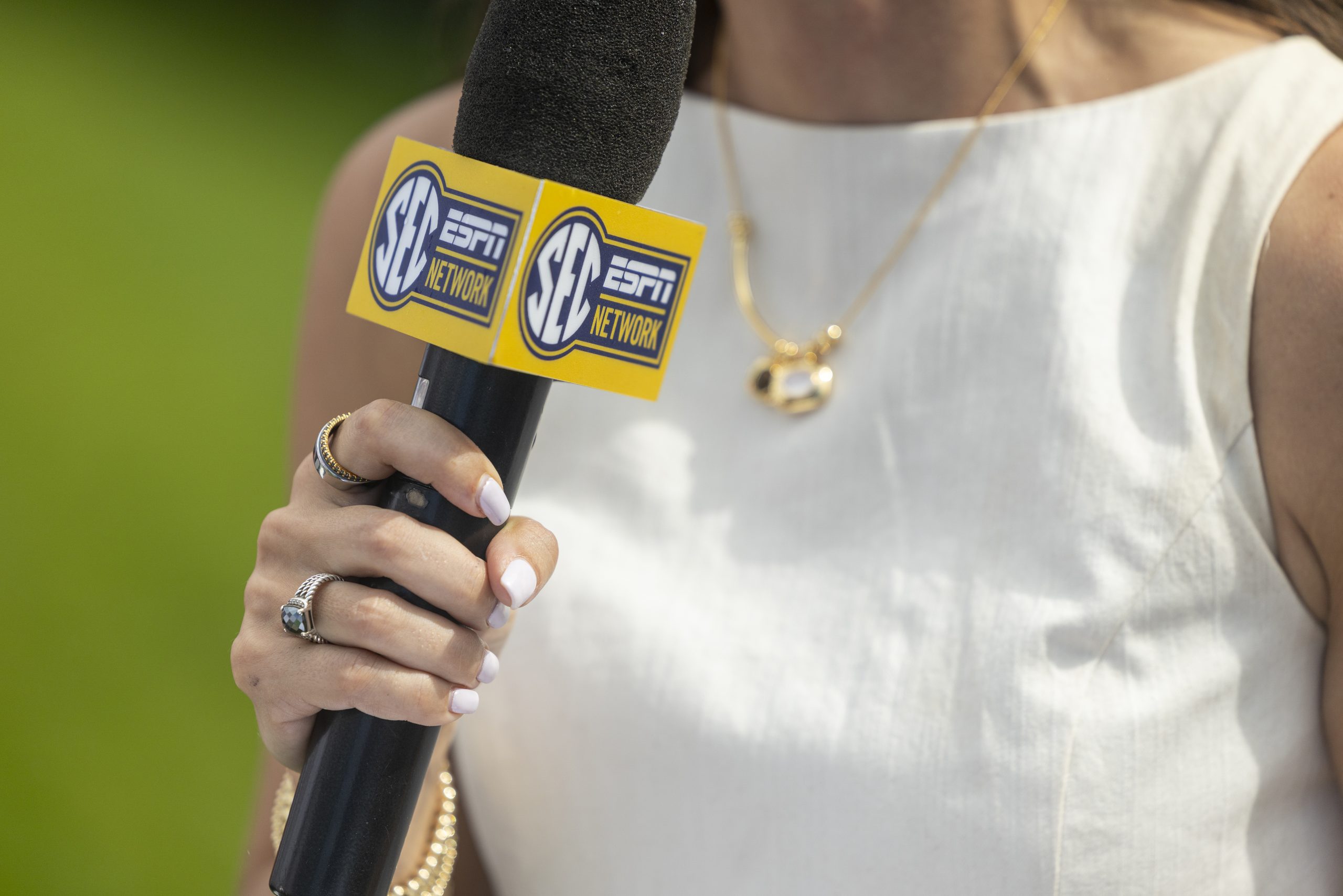 A closeup of a hand holding a microphone with a blue and yellow box around it that reads "SEC ESPN Network."