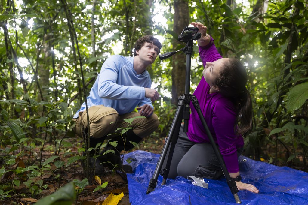 Two college students set up a camera tripod outside in a forest.
