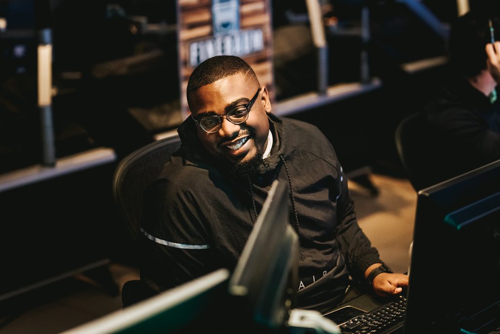A young man sits in a chair in a dark radio production room.