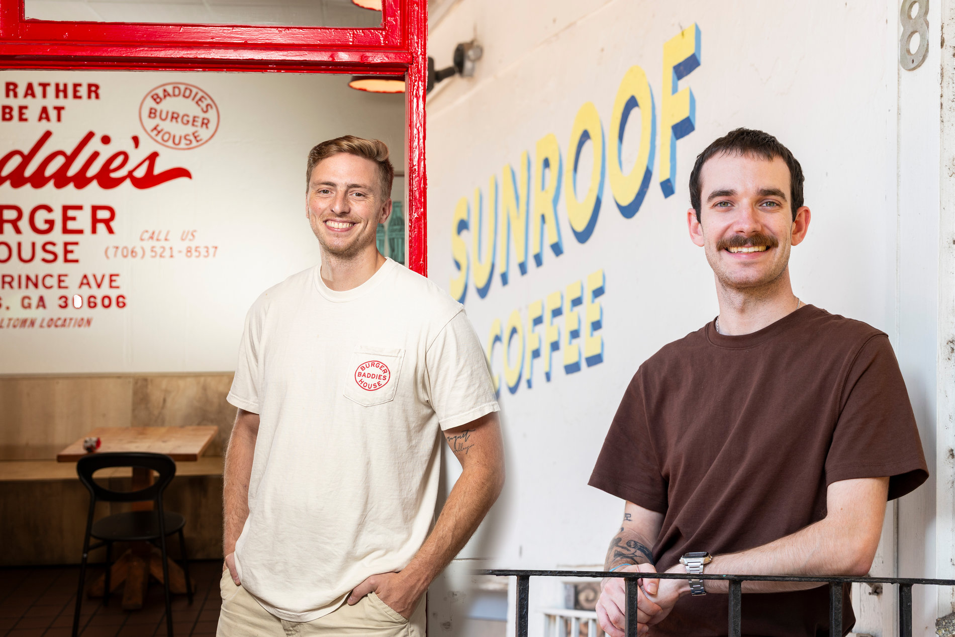 Two smiling young men pose outside a shared storefront featuring branding for Baddies Burger House and Sunroof Coffee.